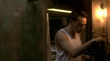 Movie still from “The Hand” (2004), directed by Kar-Wai Wong – A man in a white tank top looking at his cell phone; Medium shot, Low angle