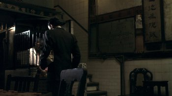 Movie still from “The Hand” (2004), directed by Kar-Wai Wong – A man in a black suit standing next to a chair; Medium shot, Over the shoulder angle