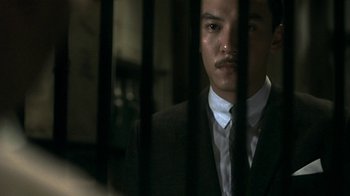 Movie still from “The Hand” (2004), directed by Kar-Wai Wong – A man wearing a suit and tie behind bars; Close Up shot, Low angle