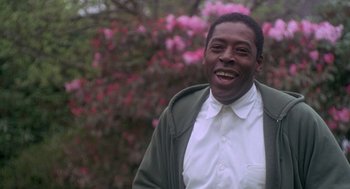 Movie still from “The Hand That Rocks the Cradle” (1992), directed by Curtis Hanson – A man smiling in front of a tree with pink flowers; Close Up shot, Low angle