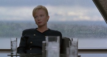 Movie still from “The Hand That Rocks the Cradle” (1992), directed by Curtis Hanson – A woman sitting at a table with a drink in front of a window; Medium shot, Over the shoulder angle