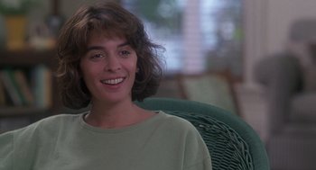 Movie still from “The Hand That Rocks the Cradle” (1992), directed by Curtis Hanson – A person sitting in a chair smiling; Close Up shot, Over the shoulder angle