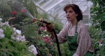 Movie still from “The Hand That Rocks the Cradle” (1992), directed by Curtis Hanson – A woman spraying flowers with a hose in a greenhouse; Medium shot, Low angle