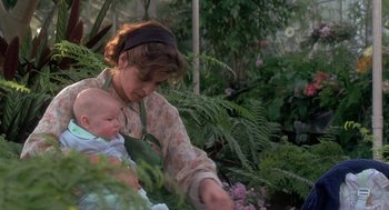 Movie still from “The Hand That Rocks the Cradle” (1992), directed by Curtis Hanson – A woman holding a baby in a garden; Medium shot, High angle