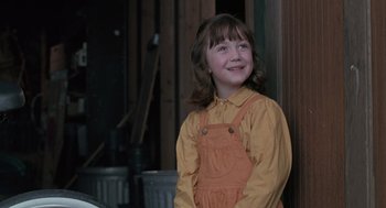Movie still from “The Hand That Rocks the Cradle” (1992), directed by Curtis Hanson – A young girl wearing an overalls smiles for the camera; Close Up shot, Over the shoulder angle