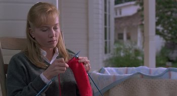Movie still from “The Hand That Rocks the Cradle” (1992), directed by Curtis Hanson – A woman knitting a red sock on a porch; Medium shot, High angle