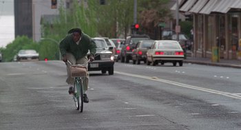 Movie still from “The Hand That Rocks the Cradle” (1992), directed by Curtis Hanson – A man riding a bike down the middle of the street; Wide shot, Low angle