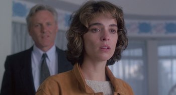 Movie still from “The Hand That Rocks the Cradle” (1992), directed by Curtis Hanson – A woman in a brown jacket and a man in a suit in the background; Close Up shot, Over the shoulder angle