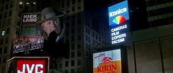 Movie still from “The Hard Way” (1991), directed by John Badham – A man wearing a hat and a fedora is in front of a building; Extreme Wide shot, Low angle