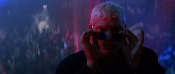 Movie still from “The Hard Way” (1991), directed by John Badham – A man in a black shirt holding a pair of sunglasses; Close Up shot, Low angle