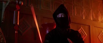 Movie still from “The Hard Way” (1991), directed by John Badham – A man in a black mask holding a red object; Medium shot, Low angle