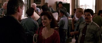Movie still from “The Hard Way” (1991), directed by John Badham – A woman in a red dress smiling in front of a group of people; Medium shot, Over the shoulder angle