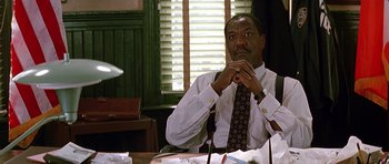 Movie still from “The Hard Way” (1991), directed by John Badham – A man sitting at a table in front of a window; Medium shot, Low angle