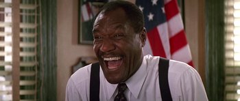 Movie still from “The Hard Way” (1991), directed by John Badham – An older black man wearing a white shirt and a tie laughing; Close Up shot, Low angle