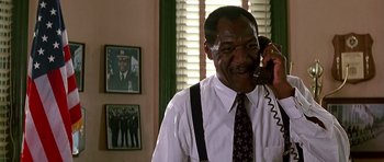 Movie still from “The Hard Way” (1991), directed by John Badham – A man talking on a phone while wearing suspenders; Medium shot, Low angle