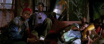Movie still from “The Hard Way” (1991), directed by John Badham – A man sitting on top of a couch in a room; Medium shot, Low angle