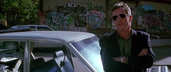 Movie still from “The Hard Way” (1991), directed by John Badham – A man in sunglasses standing in front of a car; Medium shot, Low angle