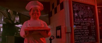 Movie still from “The Hard Way” (1991), directed by John Badham – A statue of a chef holding a plate of cake; Medium shot, Low angle
