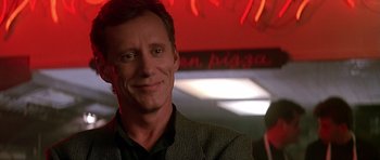 Movie still from “The Hard Way” (1991), directed by John Badham – A person wearing a suit and smiling; Close Up shot, Over the shoulder angle