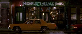 Movie still from “The Hard Way” (1991), directed by John Badham – A yellow taxi cab driving past a building with advertisments; Extreme Wide shot, Low angle