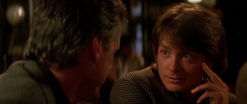 Movie still from “The Hard Way” (1991), directed by John Badham – A man and a woman sitting at a table talking to each other; Close Up shot, Over the shoulder angle