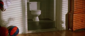 Movie still from “The Hard Way” (1991), directed by John Badham – A toilet sitting in the corner of a bathroom next to a door; Wide shot, High angle