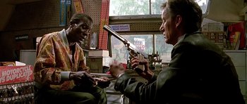 Movie still from “The Hard Way” (1991), directed by John Badham – Two men sitting in front of each other holding a gun; Medium shot, Low angle