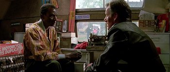 Movie still from “The Hard Way” (1991), directed by John Badham – Two men sitting in front of a tv in a room; Medium shot, Over the shoulder angle