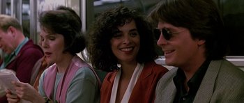 Movie still from “The Hard Way” (1991), directed by John Badham – A woman smiles while standing next to two other people; Close Up shot, Over the shoulder angle