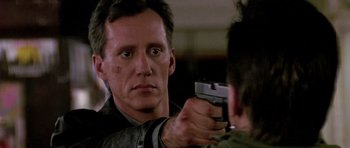 Movie still from “The Hard Way” (1991), directed by John Badham – A man holding a gun pointed at another man's face; Close Up shot, Over the shoulder angle