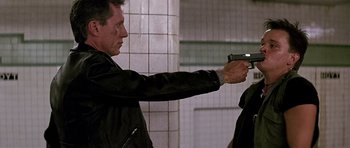 Movie still from “The Hard Way” (1991), directed by John Badham – A man holding a gun while standing next to another man; Medium shot, Over the shoulder angle