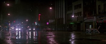 Movie still from “The Hard Way” (1991), directed by John Badham – A car driving down a wet street at night; Extreme Wide shot, High angle