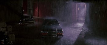 Movie still from “The Hard Way” (1991), directed by John Badham – A car is driving in the rain at night; Wide shot, High angle