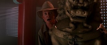 Movie still from “The Hard Way” (1991), directed by John Badham – A man in a hat is standing next to a statue; Medium shot, Low angle