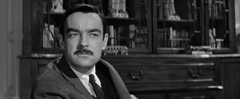 Movie still from “The Haunting” (1963), directed by Robert Wise – A man in a suit and tie in front of bookcases; Close Up shot, Over the shoulder angle