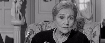 Movie still from “The Haunting” (1963), directed by Robert Wise – An older woman sitting on a couch looking at the camera; Close Up shot, Over the shoulder angle