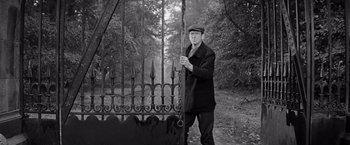 Movie still from “The Haunting” (1963), directed by Robert Wise – A black and white photo of a man standing next to an iron gate; Medium shot, Low angle