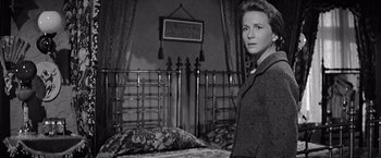Movie still from “The Haunting” (1963), directed by Robert Wise – A black and white photo of a woman standing in front of a bed; Medium shot, High angle