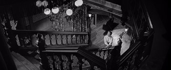 Movie still from “The Haunting” (1963), directed by Robert Wise – A man sitting on a railing of a staircase; Wide shot, High angle