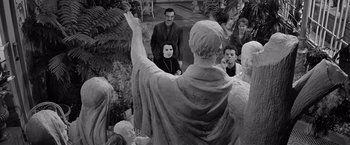 Movie still from “The Haunting” (1963), directed by Robert Wise – A group of people standing around a statue; Wide shot, Over the shoulder angle
