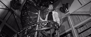 Movie still from “The Haunting” (1963), directed by Robert Wise – A black and white photo of a man on top of a spiral staircase; Medium shot, Low angle