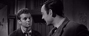 Movie still from “The Haunting” (1963), directed by Robert Wise – Two men in suits talking to each other in front of a wooden wall; Close Up shot, Over the shoulder angle