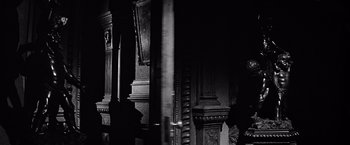 Movie still from “The Haunting” (1963), directed by Robert Wise – A black - and - white photo of a room with pillars; Medium shot, Over the shoulder angle