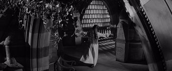 Movie still from “The Haunting” (1963), directed by Robert Wise – A woman in a long white dress dancing in front of an archway; Wide shot, High angle