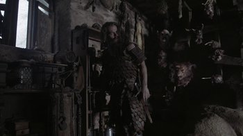 Movie still from “The Head Hunter” (2018), directed by Jordan Downey – A man dressed as a viking in a dark room; Medium shot, Over the shoulder angle