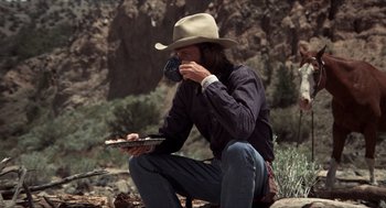 Movie still from “The Hired Hand” (1971), directed by Peter Fonda – A man sitting on the ground wearing a cowboy hat; Wide shot, Low angle