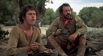 Movie still from “The Hired Hand” (1971), directed by Peter Fonda – Two men sitting on the ground eating food; Medium shot, Low angle