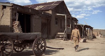 Movie still from “The Hired Hand” (1971), directed by Peter Fonda – A man walking down a dirt road near a building; Wide shot, Low angle