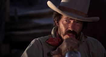 Movie still from “The Hired Hand” (1971), directed by Peter Fonda – A man in a cowboy hat and a neck tie holding a bottle; Close Up shot, Low angle