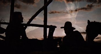 Movie still from “The Hired Hand” (1971), directed by Peter Fonda – A man wearing a hat sitting in front of a wooden structure; Wide shot, Low angle
